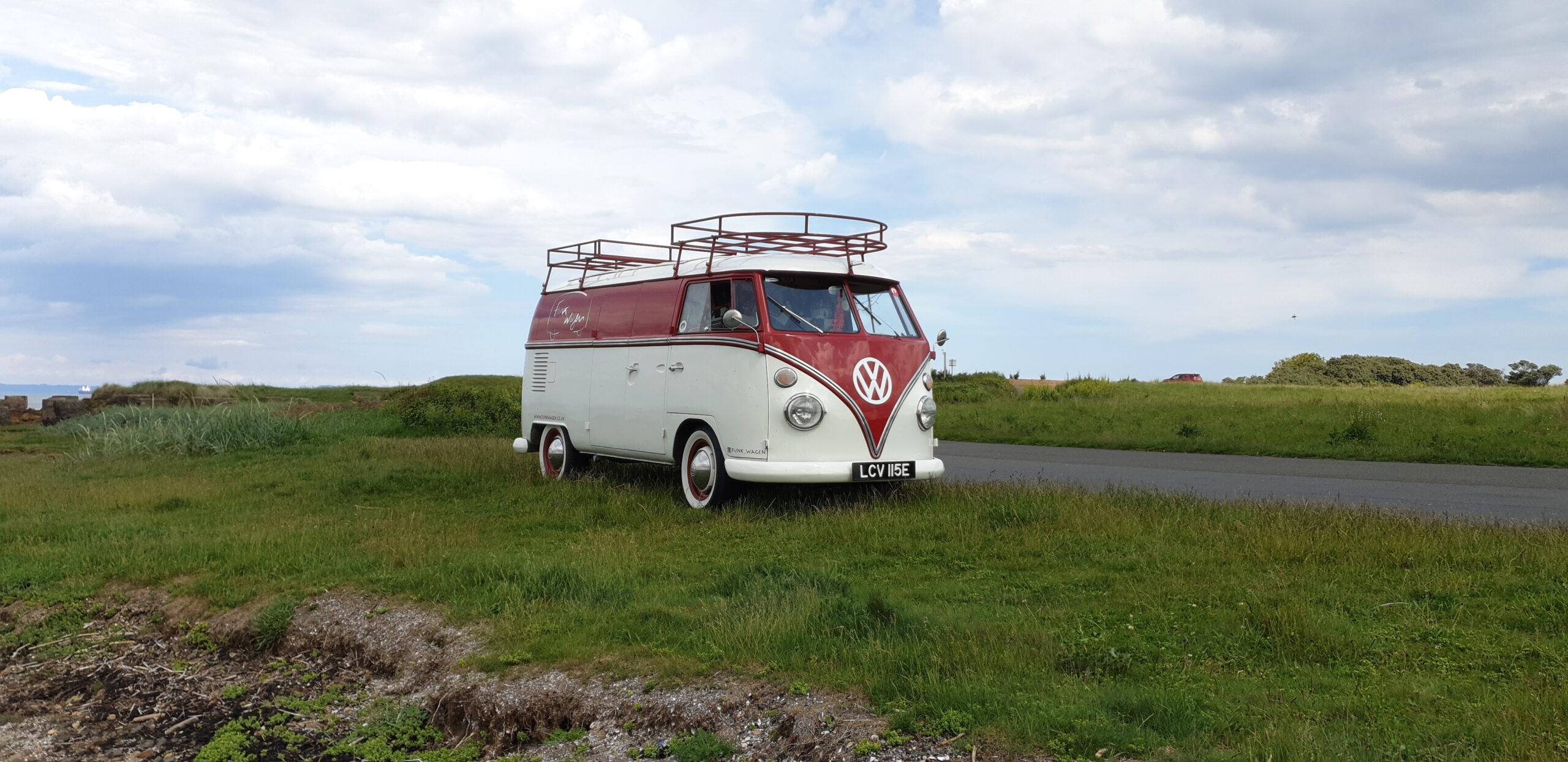 The Funkwagen, a red and white 1967 VW split-screen camper, parked on the grass beneath a big Scottish sky